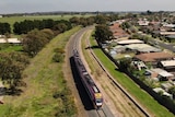 A drone photo of a three-carriage Vline train travelling past homes on a section of single track.