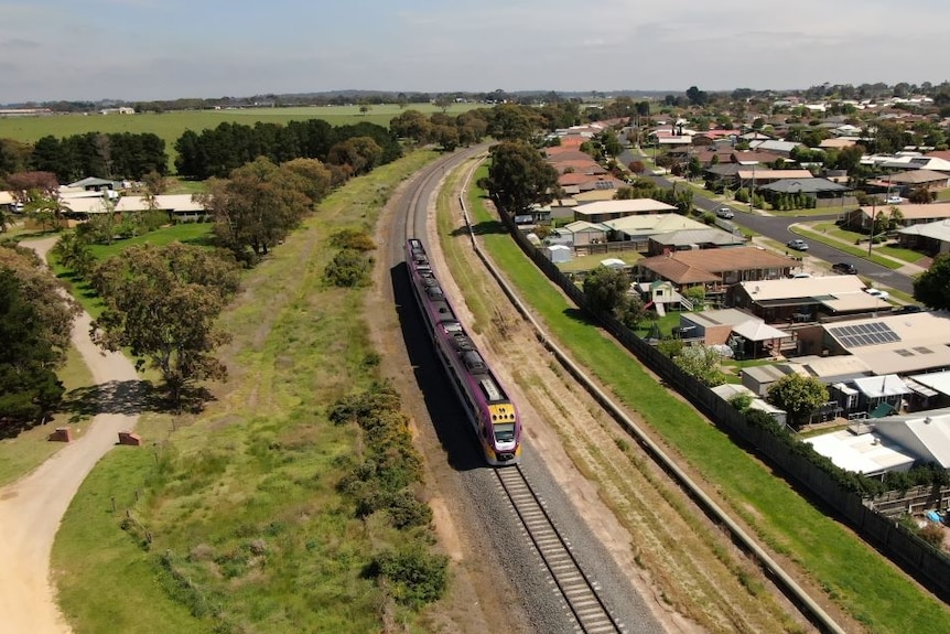 A drone photo of a three-carriage Vline train travelling past homes on a section of single track.