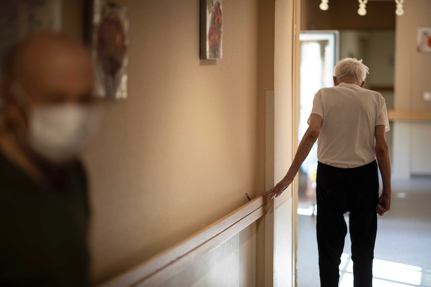 An elderly man walks with the assistance of a hand rail.