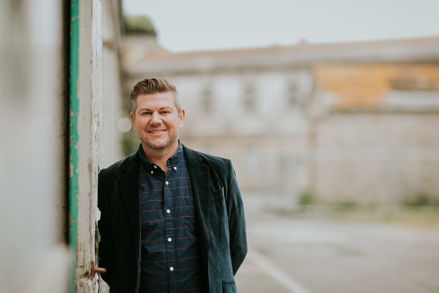 Wayne Knapman wearing a blazer, leans against a wall.