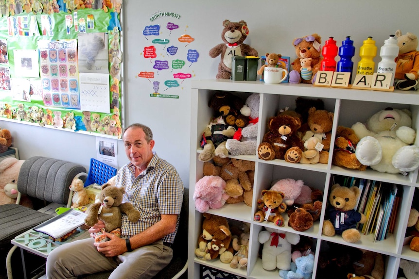 A man sits holding a teddy bear in a room full of teddy bears