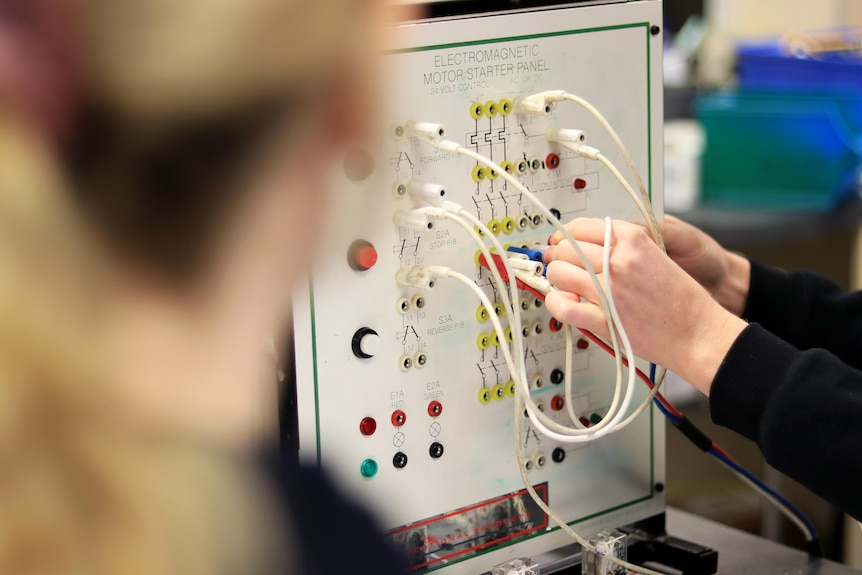 A close-up of an electrical panel with cords coming out of it and hands pushing cords in.