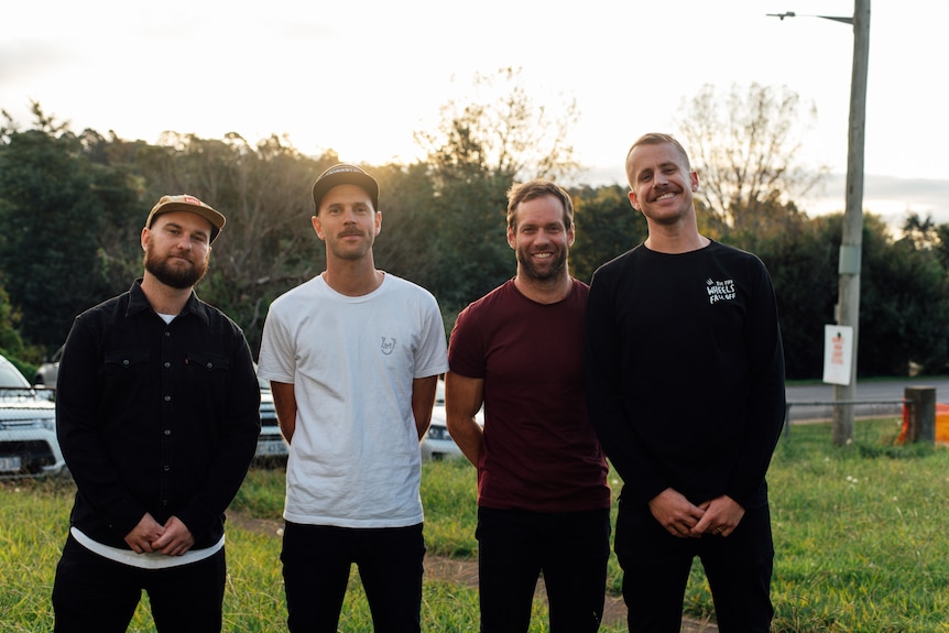 Four men standing in a line in a park.