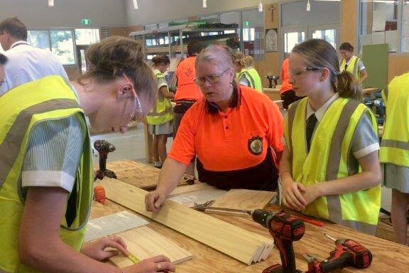 Fi Shewring, founder of Supporting and Linking Tradeswomen, watches over two highschool girls measuring wood.