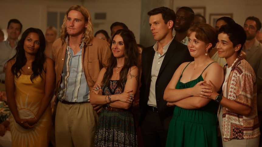 A TV still of Pooja Shah, Conor Merrigan-Turner, Alison Brie, Jake Lacy, Essie Randles and Paula Andrea Placido in a row.