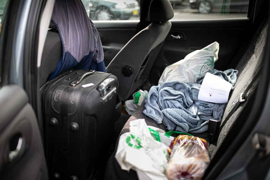 A suitcase and clothes on the backseat of a car