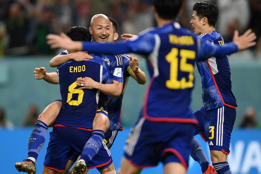 Football players in blue shirts hugging in celebration. 