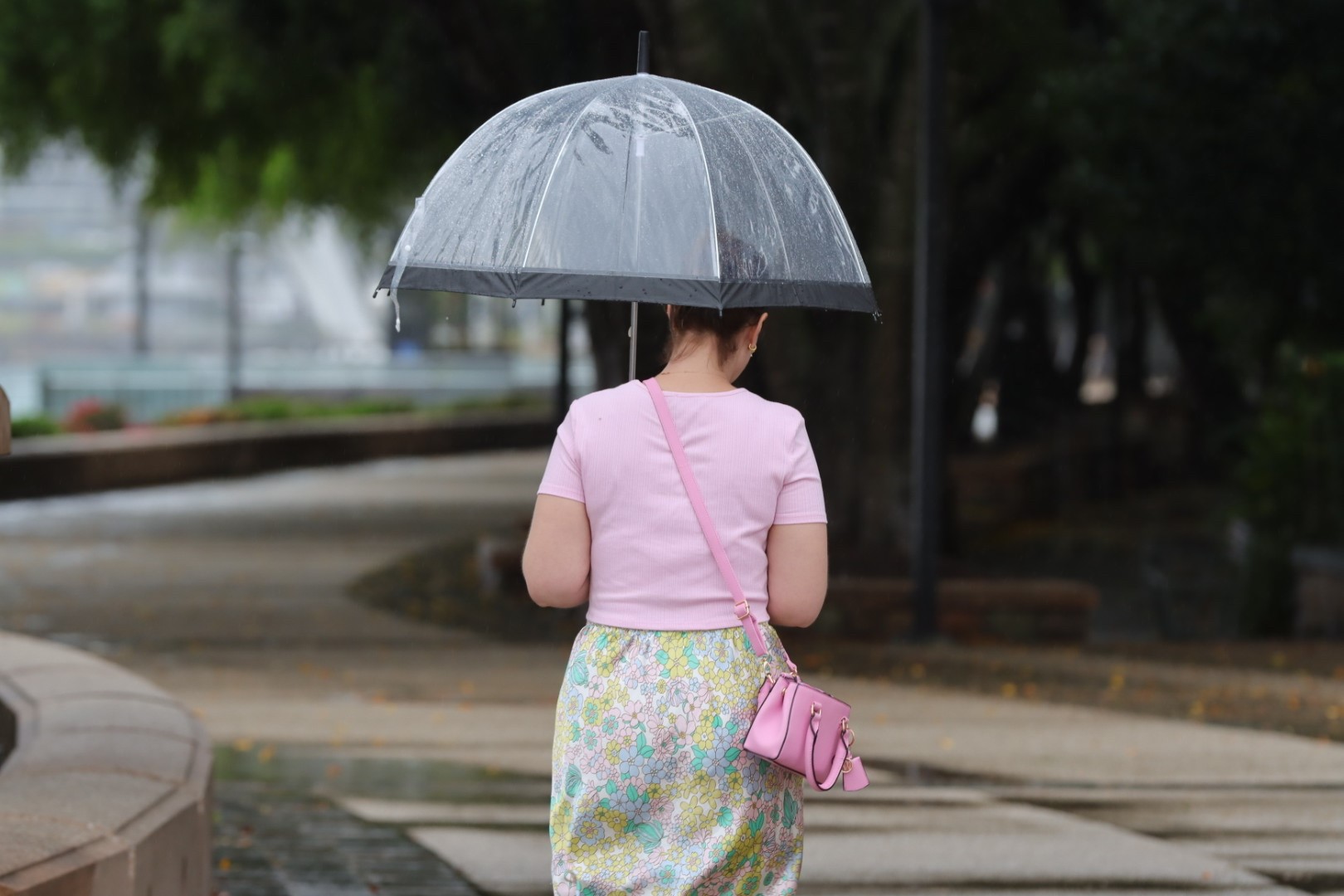 Una mujer vestida con un top rosa y una falda floral camina bajo un paraguas bajo la lluvia en Brisbane.