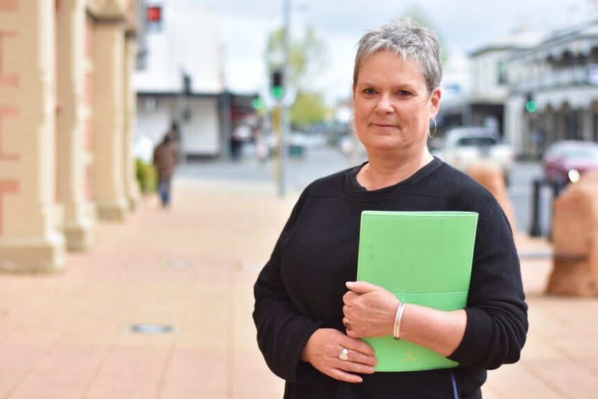 A woman with short grey hair wearing a black top holds a book in a Mount Gambier street.