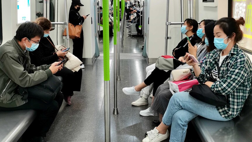 People sitting on a subway wearing masks and looking at phones.
