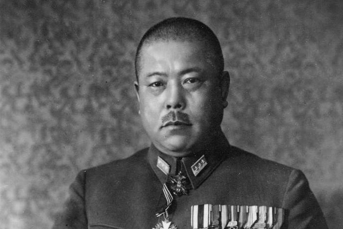 A black and white photo of a Japanese man with a buzzcut dressed in a dress military uniform, holding a sword