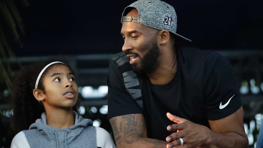 Kobe Bryant looks at his daughter Gianna while leaning on a barrier