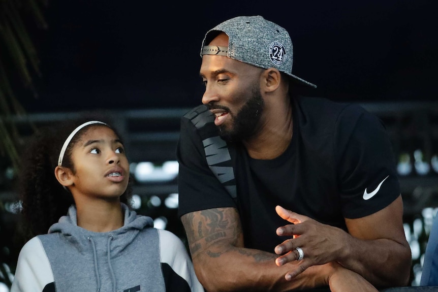 Kobe Bryant looks at his daughter Gianna while leaning on a barrier