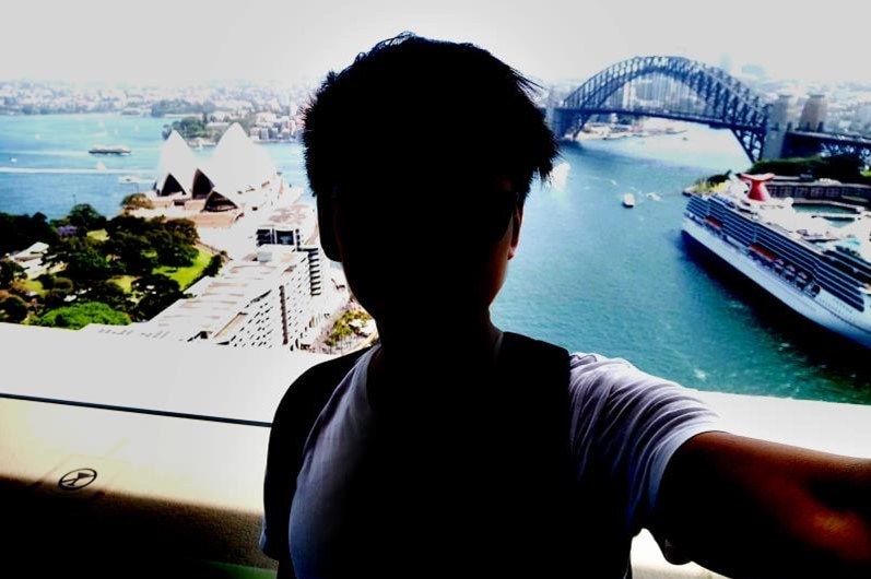 A photo of a person overlooking the Sydney Harbour Bridge and Opera House with face in shadow.