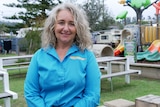 A smiling woman with long grey hair stands in a caravan park.