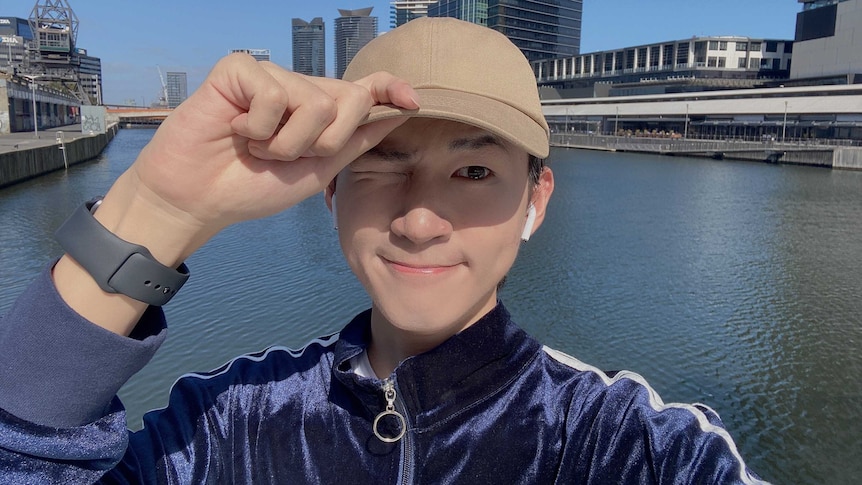 A Chinese man in his 20s holding his hat in Melbourne's Southbank