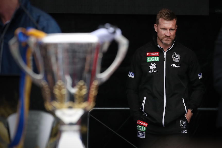 Nathan Buckley looks on at the 2018 premiership cup in the foreground with West Coast coloured ribbons