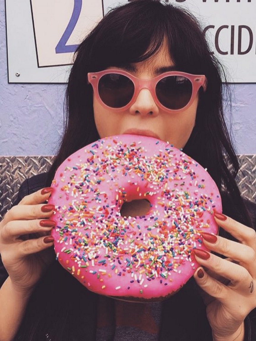 A woman bites into a large, pink iced donut.