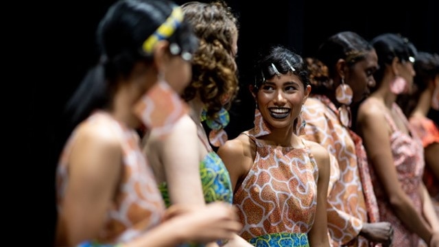 Models talk to each other while wearing Indigenous fashion.
