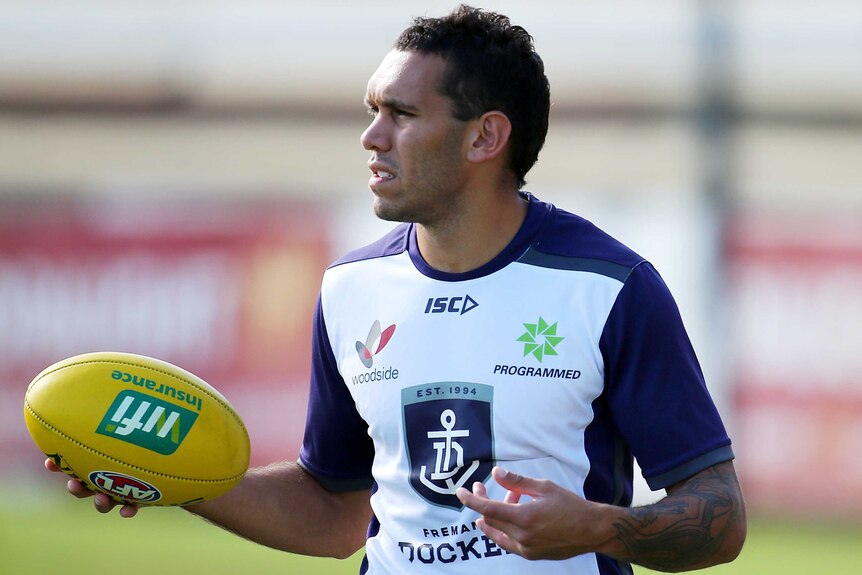 Harley Bennell walks laps at training wearing a white Fremantle Dockers shirt and holding a yellow football.