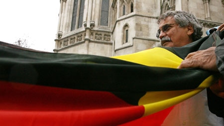 Clyde Mansell from the Tasmanian Aboriginal Council holds an Aboriginal flag