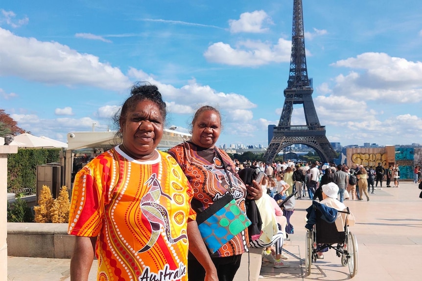 Two Indigenous women in colourful t-shirts pose in front of the Eiffel Tower