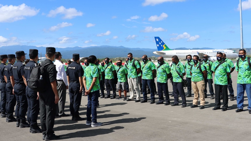 Chinese police stand in navy uniforms opposite Solomon Islands police wearing bright green island tops on an airport tarmac 