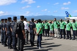 Chinese police stand in navy uniforms opposite Solomon Islands police wearing bright green island tops on an airport tarmac 