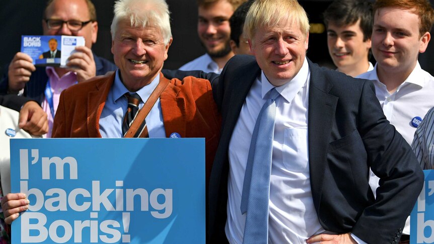A man in a suit puts his arm around an older man holding a sign reading "I'm backing Boris"
