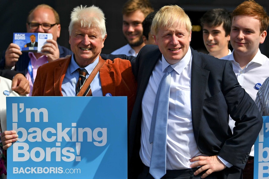 A man in a suit puts his arm around an older man holding a sign reading "I'm backing Boris"