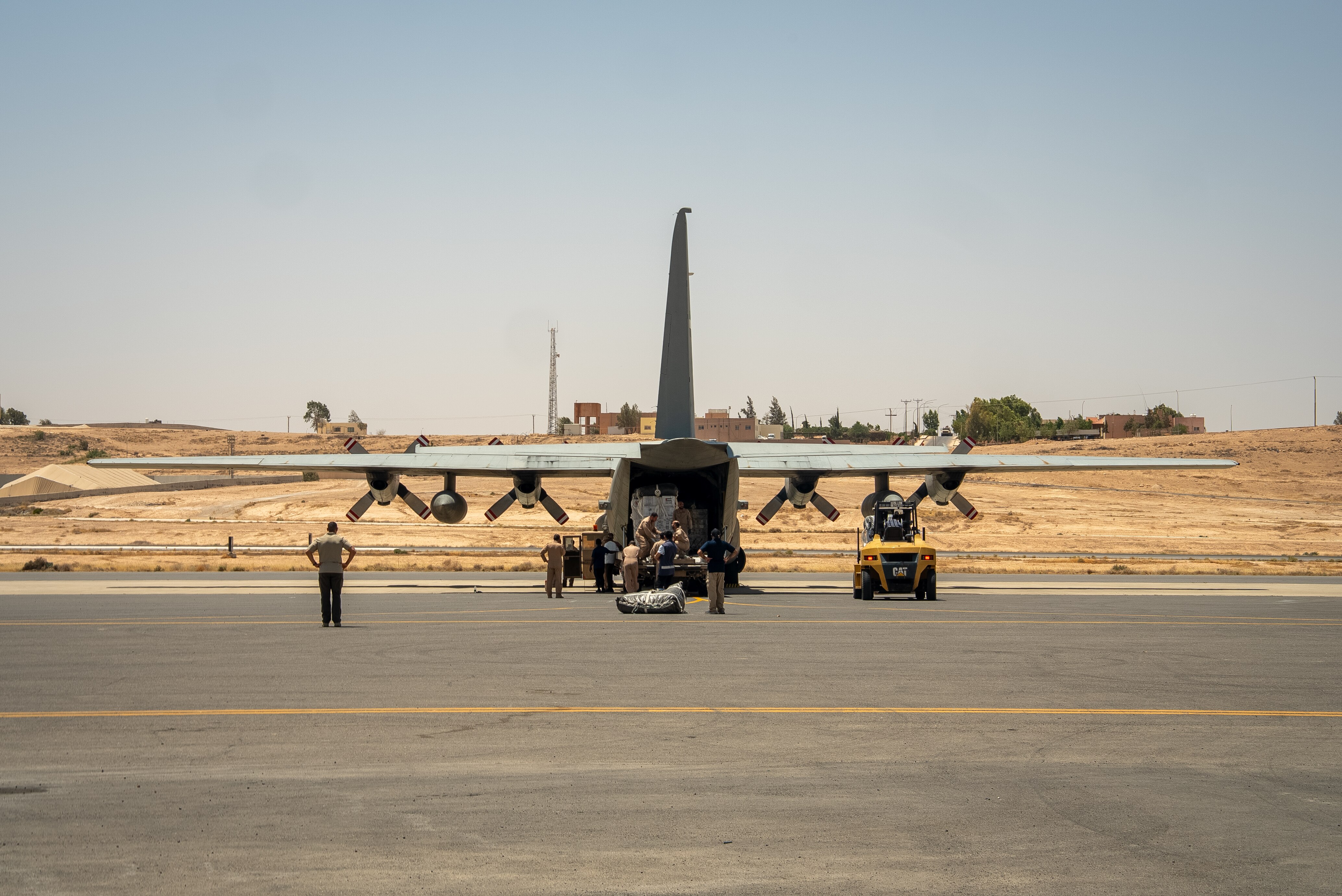 Pallets of aid are loaded into the rear of a military cargo plane with four propellers.