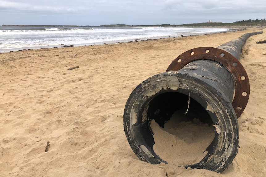 Dredge pipe on beach, sea in the background. Cloudy sky.