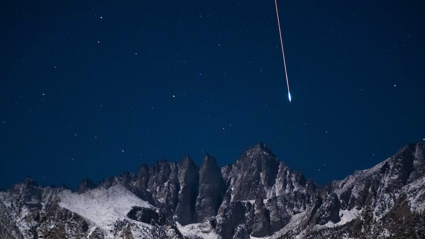 A meteor falls from the sky over a dramatic mountain range.