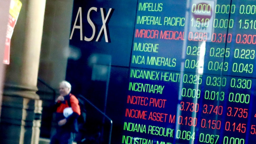 A man in his-vis gear walks past an ASX share price board.