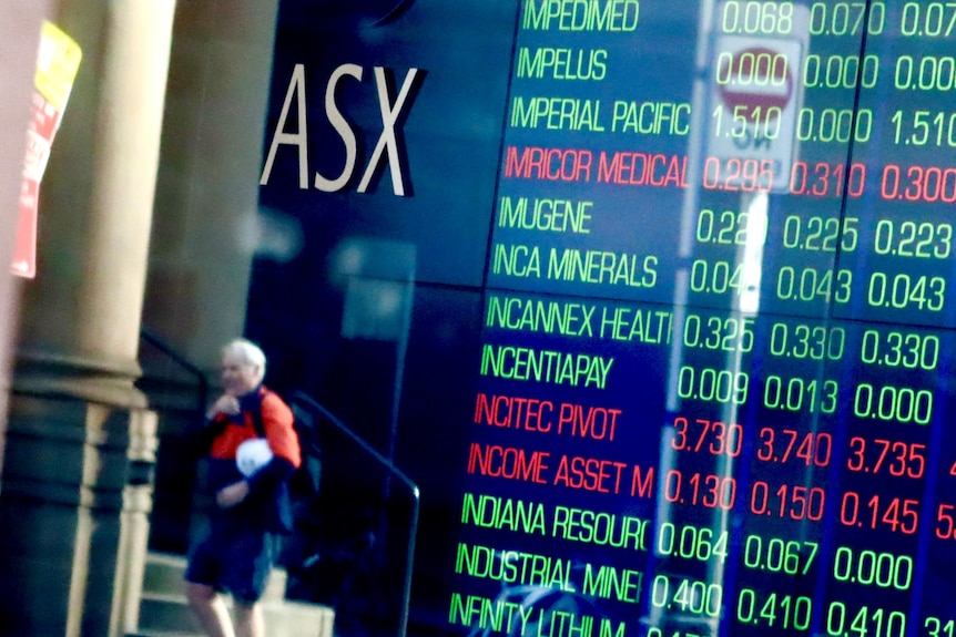 A man in his-vis gear walks past an ASX share price board.
