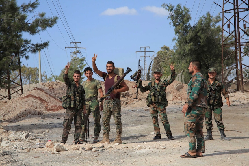Forces loyal to Syria's President Bashar al-Assad flash victory signs as they stand at a military complex.