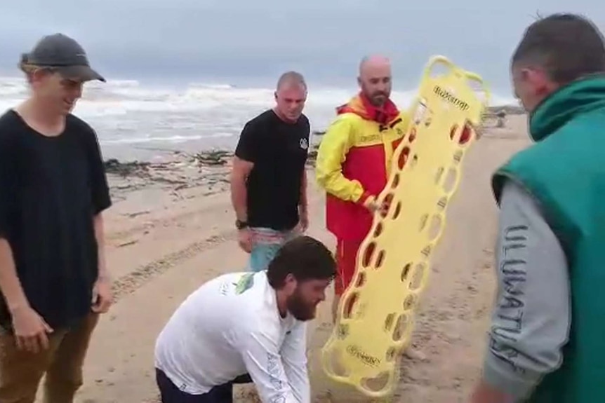 A lifesaver carrying a long yellow spinal board.