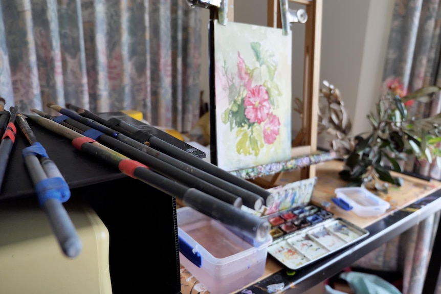 Home painting studio with special longer brushes in foreground and painting of flowers in background