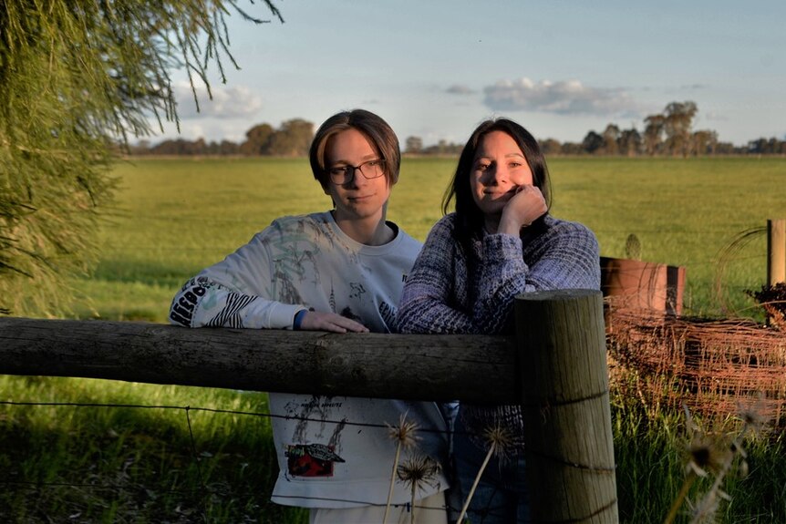 A woman and a teenage boy resting on a farm fence 