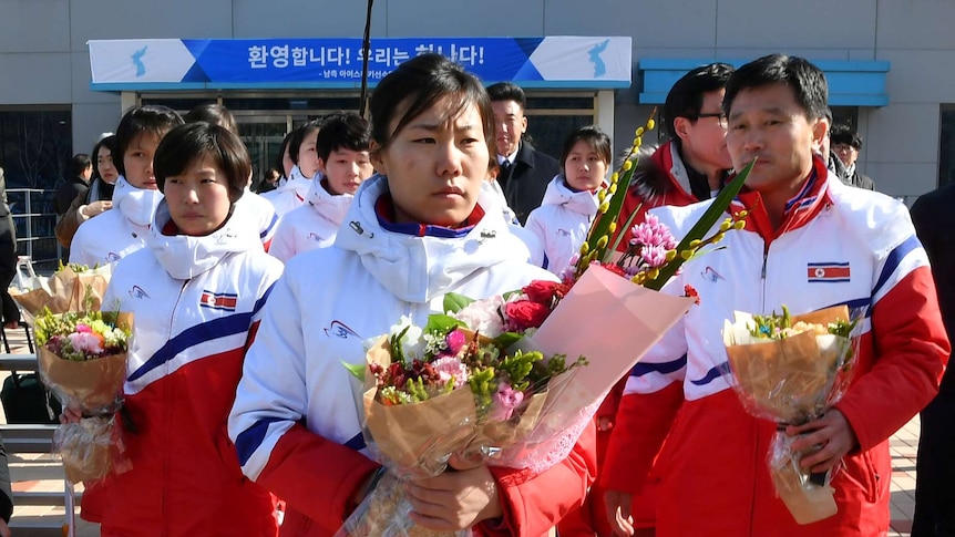 North Korean women's ice hockey players wearing uniforms hold bunches of flowers.