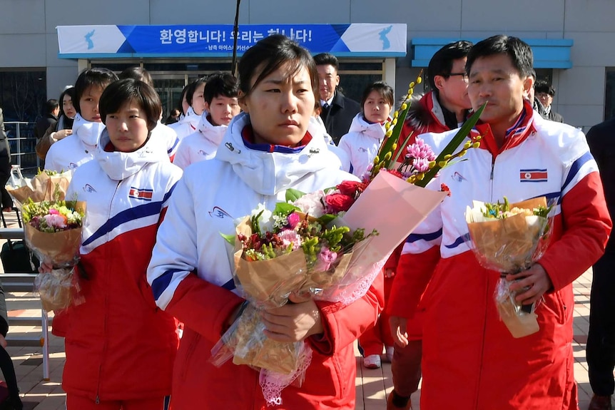 North Korean women's ice hockey players wearing uniforms hold bunches of flowers.