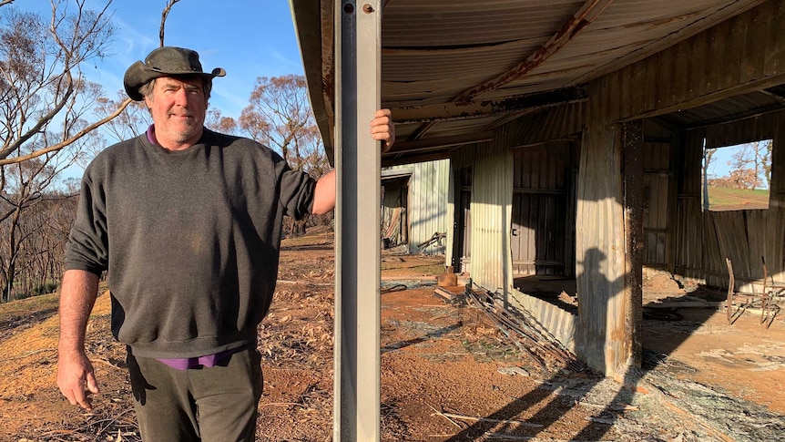 Barry Smith standing next to a fire-damaged building on Kangaroo Island