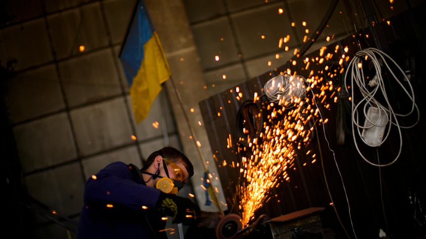 Young man wearing a protective mask in an industrial setting using an angle grinder, creating sparks.