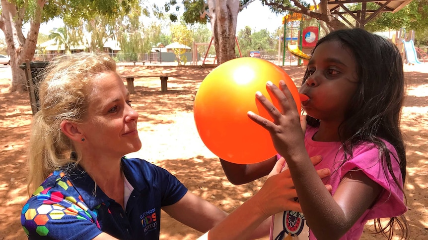 Woman with girl who is blowing up a balloon