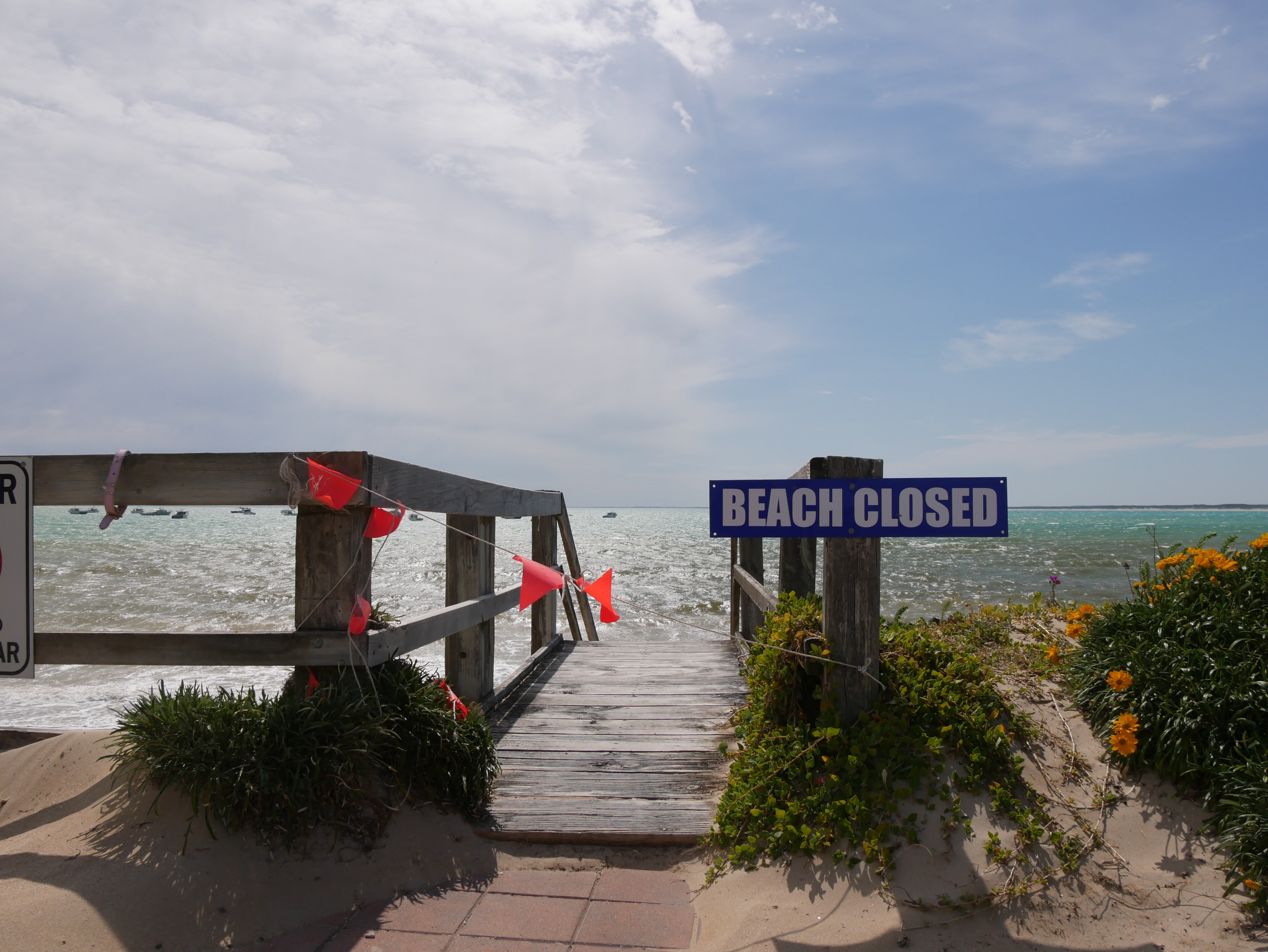 A sign which says beach closed in front of stairs leading to a beach. 
