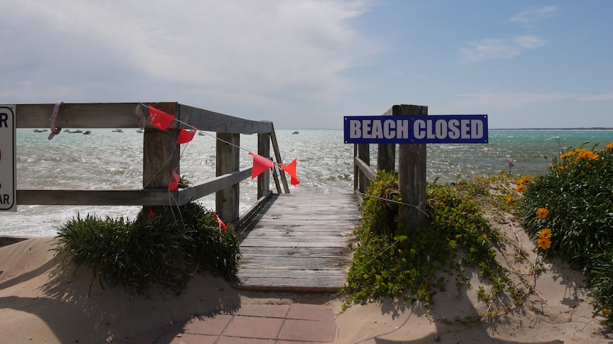 A sign which says beach closed in front of stairs leading to a beach. 