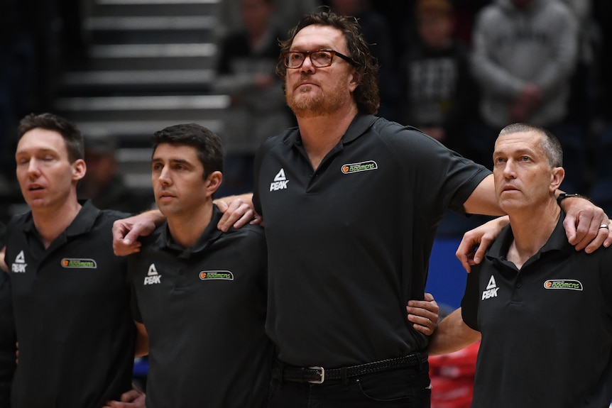 Four male Boomers staff stand with their arms on each other's shoulders, all wearing  black polo shirts