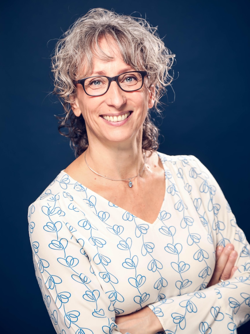 A headshot of a woman with short light hair and glasses. She's crossing her arms and smiling.