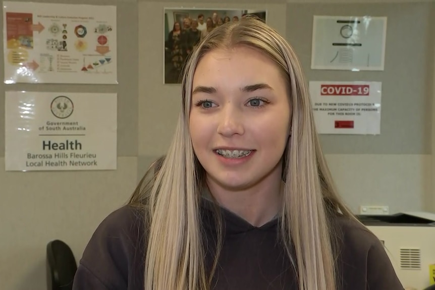 A young girl with blonde hair smile as she sits in a doctor's clinic