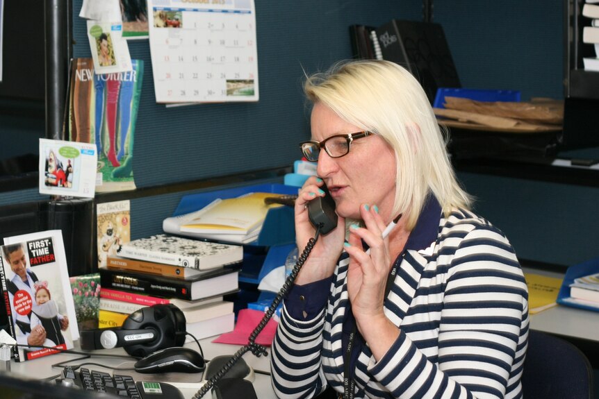 Woman with blond hair, dark rimmed glasses and a striped top talks on the telephone 